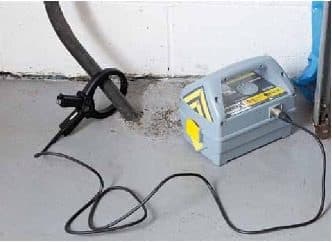 A signal clamp around a cable where it runs down a wall into the floor, with the Genny alongside