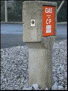 A concrete post at the roadside carrying a gas emergency control point box marked GAS, standing in gravel.