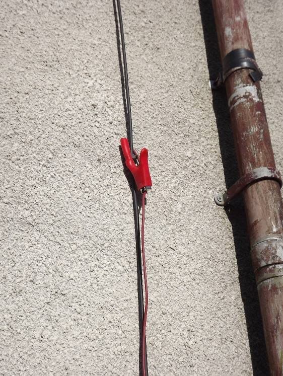 Red clip on a cable running down a rendered wall beside an old iron pipe.