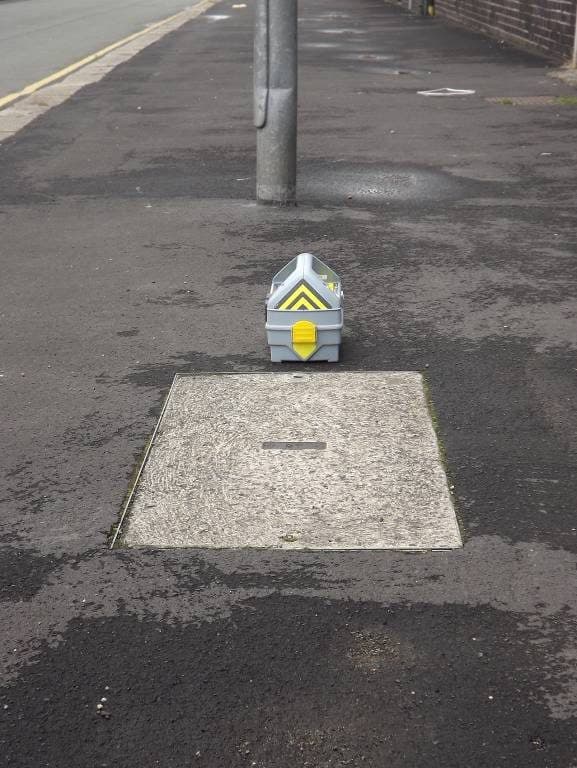 Genny stood upright on the footway in line with a chamber cover: induction position.